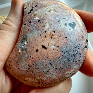 Polished Ocean Jasper moon in warm pink and tan tones with starburst orbicular markings held in hand