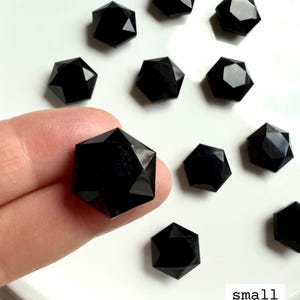 Mini Black Obsidian hexagon crystal balanced on fingertips for size reference, polished gemstone for grounding and energetic shielding