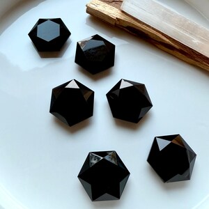 Polished Black Obsidian faceted hexagons arranged on a white dish beside Palo Santo — protective root chakra crystals for grounding and energetic shielding.
