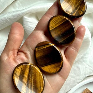 hand holding tiger’s eye worry stone showing silky golden brown banding, crystal for confidence courage and grounding energy
