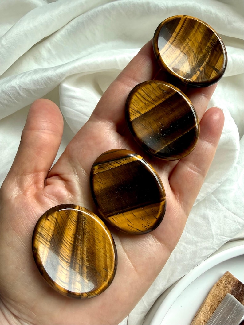 hand holding tiger’s eye worry stone showing silky golden brown banding, crystal for confidence courage and grounding energy