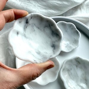 Close-up of hand holding a white marble daisy bowl showing natural gray and white stone patterning