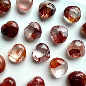 May include: A collection of heart-shaped red and clear quartz crystals. The crystals are polished and have a natural, raw look.