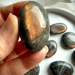 Peach Sunset Labradorite palm stone held in hand with vibrant orange, peach, and golden flash