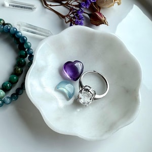 White marble daisy bowl with scalloped flower edges holding an amethyst heart carving, aquamarine moon carving, and silver ring