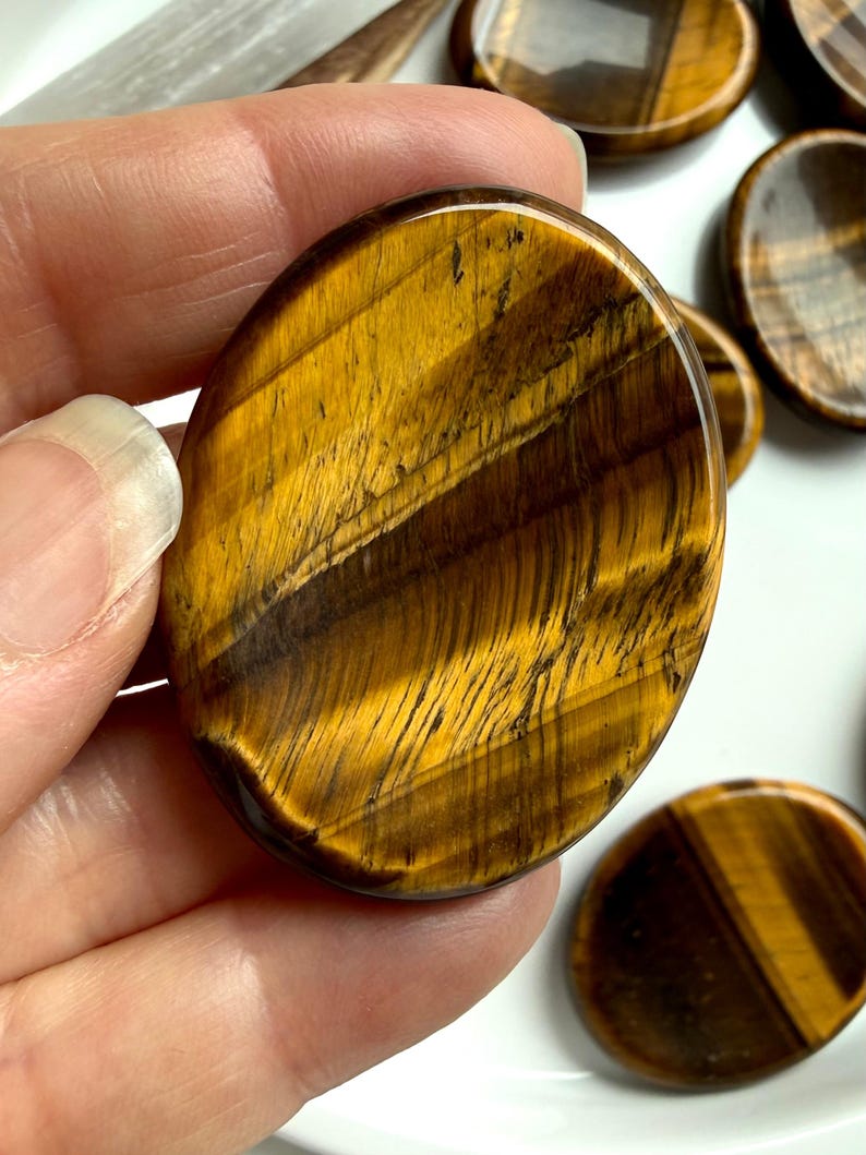 tiger’s eye worry stone held between fingers showing natural banding and sheen, crystal for protection strength and balance