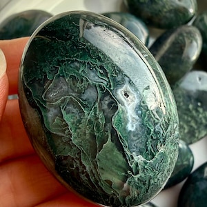 Moss agate palm stone held in hand, polished grounding crystal with green moss inclusions for calm and stability