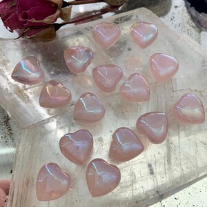 Mini aura rose quartz hearts on a selenite slab with dried roses — glowing pink crystals for love, healing & heart-centered rituals