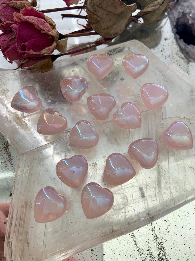 Mini aura rose quartz hearts on a selenite slab with dried roses — glowing pink crystals for love, healing & heart-centered rituals