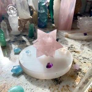 Round selenite plate as a display base for large rose quartz merkaba carving, styled within crystal collection
