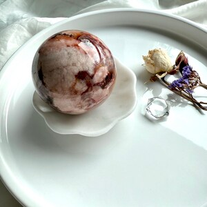 White marble daisy bowl holding a 56mm polished crystal sphere for display, styled with dried flowers and a clear quartz hexagon