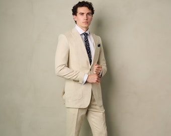May include: A man wearing a light beige linen suit with a white shirt and a dark blue patterned tie. He is wearing white sneakers.