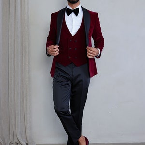 Pu&ograve; includere: Un abito in velluto bordeaux con revers in raso nero e un gilet in velluto bordeaux abbinato. L'abito &egrave; indossato con una camicia bianca e un papillon nero. Il modello indossa mocassini in velluto bordeaux.