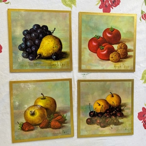 Pode incluir: Quatro pinturas quadradas com moldura dourada de arranjos de frutas de natureza morta. A pintura no canto superior esquerdo mostra um cacho de uvas roxas e uma pêra amarela. A pintura no canto superior direito mostra três tomates vermelhos e duas nozes. A pintura no canto inferior esquerdo mostra duas maçãs amarelas e três morangos vermelhos. A pintura no canto inferior direito mostra um cacho de cerejas vermelho-escuro e duas peras amarelas.