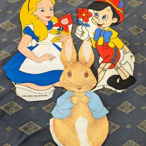 May include: Three fabric panels featuring printed illustrations of Alice, Pinocchio, and Peter Rabbit. Each character is depicted in full color with white borders and text at the bottom that reads LEAVE OPEN FOR STUFFING for sewing projects.