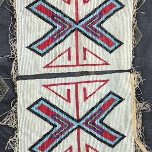 Op de afbeelding: Twee rechthoekige kralenpanelen met een witte achtergrond en een centraal geometrisch patroon in rood, lichtblauw, zwart en geel. Elk paneel toont een symmetrisch, kruisachtig ontwerp met gerafelde randen aan de zijkanten.