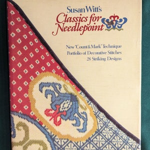 May include: Book cover for "Susan Witt's Classics for Needlepoint" featuring a colorful needlepoint design with a blue flower and a red and white background. The book title is in a decorative font and the subtitle is "New 'Count & Mark' Technique, Portfolio of Decorative Stitches, 28 Striking Designs."