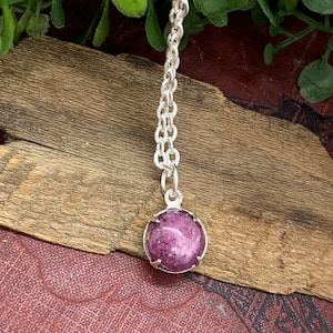 May include: A silver chain necklace with a round, pink, sparkly pendant.