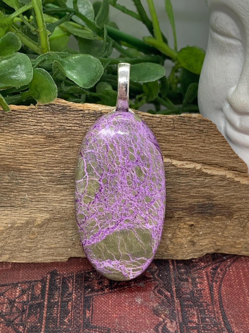 May include: An oval pendant with a silver bail, featuring a marbled pattern in shades of purple and green.