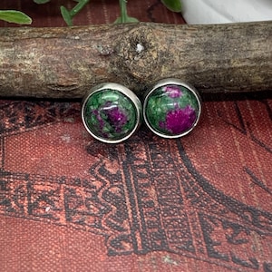May include: A pair of silver stud earrings with green and pink gemstone accents.