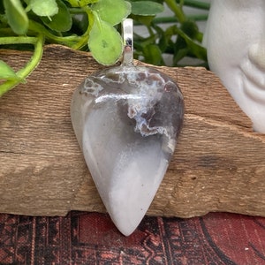 May include: A teardrop-shaped pendant made of white agate with brown and gray inclusions. The pendant has a silver bail.