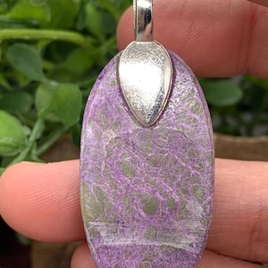 May include: An oval pendant with a silver bail, featuring a marbled pattern in shades of purple and green. A white streak runs through the centre of the pendant.