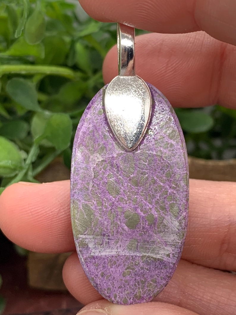 May include: An oval pendant with a silver bail, featuring a marbled pattern in shades of purple and green. A white streak runs through the centre of the pendant.