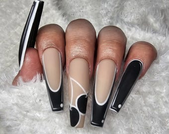 Pode incluir: Uma mão exibindo unhas de acrílico longas em forma de caixão. As unhas apresentam um design em preto e branco, com algumas unhas exibindo uma base nude com detalhes em preto e branco. Uma unha tem um design de cereja.