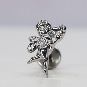 Può includere: Un piercing per il corpo in metallo argentato con una scultura dettagliata di un cupido alato con un alone a forma di cuore. Il cupido è raffigurato in una posa di volo, con un'ala distesa e l'altra ripiegata dietro la schiena. Il cupido tiene un cuore tra le mani.