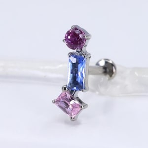 Può includere: Un orecchino argentato con tre pietre preziose colorate. Presenta una pietra rotonda viola scuro in alto, una pietra blu rettangolare al centro e una pietra rosa rettangolare in basso. L'orecchino ha una chiusura a perno.