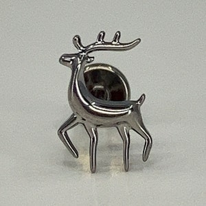 May include: A silver metal reindeer pin with a detailed design. The reindeer is standing on four legs and has a curved neck with antlers.