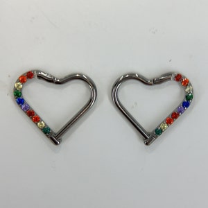 May include: Two silver heart-shaped hoop earrings with a rainbow of colourful gemstones.