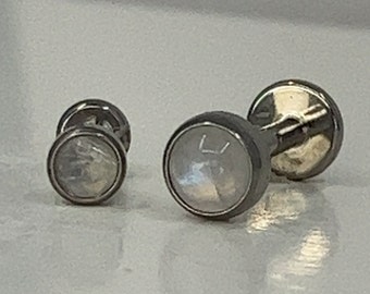 Pode incluir: Um par de botões de punho de prata com incrustações de madrepérola branca. Os botões de punho têm um design simples e são perfeitos para adicionar um toque de elegância a qualquer roupa.