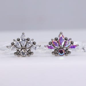 May include: Two decorative earrings with a floral design. One earring features clear, marquise-cut stones and a central round stone. The other earring has iridescent, purple-toned stones and a central, round, iridescent stone. Both earrings have a silver-coloured metal base.