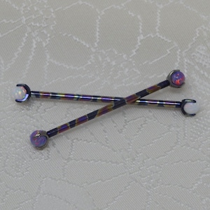 May include: Two iridescent purple and gold titanium barbell body jewelry with opal ends. One end is a white opal and the other is a pink opal.