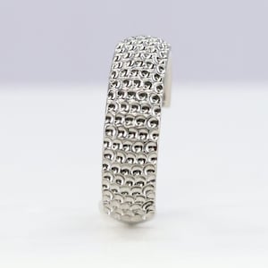 Puede incluir: Una pulsera de plata con un diseño texturizado y estampado. La pulsera está hecha de metal y tiene un acabado liso y pulido.