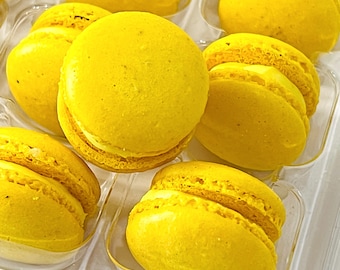 May include: A close-up of a box of yellow macarons. The macarons are arranged in a clear plastic container.