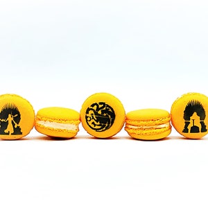 May include: Five yellow macarons with black designs. The designs include a dragon, a crown, a person, and a castle.