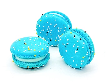 Può includere: Tre macarons blu con codette bianche e nere. I macarons sono disposti a forma di triangolo su una superficie bianca.