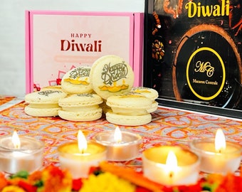 May include: A box of macarons with a Happy Diwali design. The macarons are arranged in a circle around a small box with a Happy Diwali design. There are also small candles lit around the macarons.