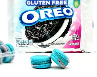 Può includere: Una confezione di biscotti Oreo al cioccolato ripieni, senza glutine, con un logo blu e bianco. Due macarons blu e grigi sono in primo piano.