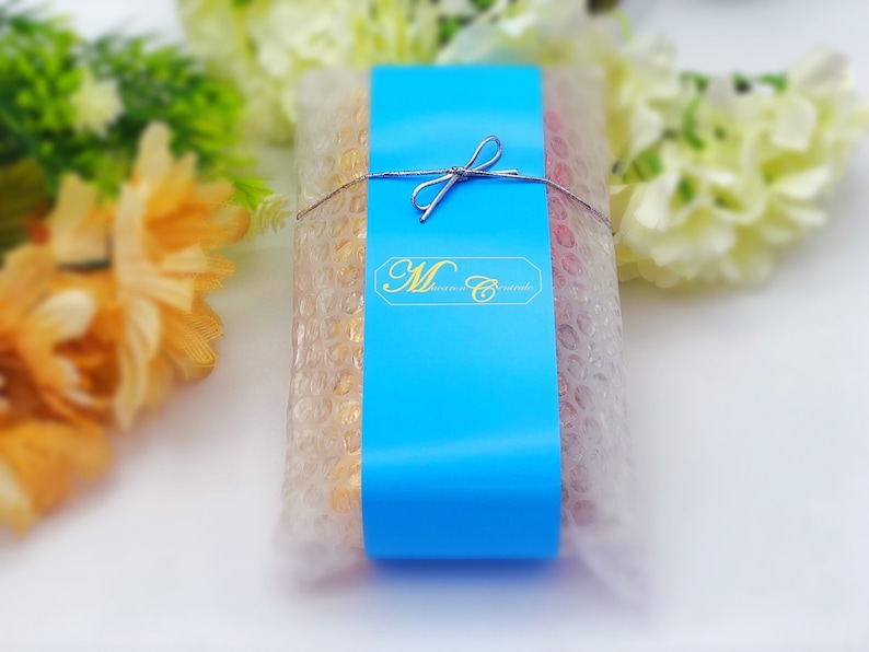 May include: A blue and white gift box with a white ribbon and bow. The box is wrapped in clear plastic with bubble wrap. The box has the text "M. Sweets" on the front.