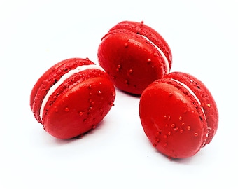 Può includere: Tre macarons rossi con ripieno bianco e codette rosse.