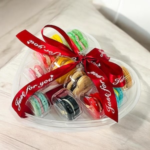 May include: A heart-shaped clear plastic container filled with colorful macarons. The container is tied with a red ribbon with the text "Just for you" printed on it.