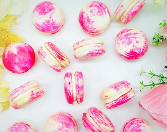 Può includere: Una collezione di macarons rosa e bianchi con un motivo a spirale. I macarons sono disposti su una superficie bianca.