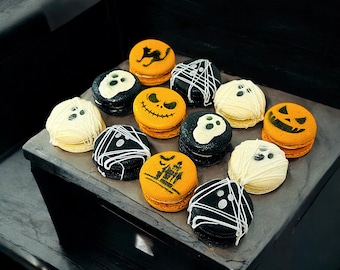 Könnte beinhalten: Eine Sammlung von Halloween-Macarons mit verschiedenen Designs, darunter Geister, Kürbisse, Schädel und ein Spukhaus. Die Macarons sind auf einem schwarzen Tablett angeordnet.