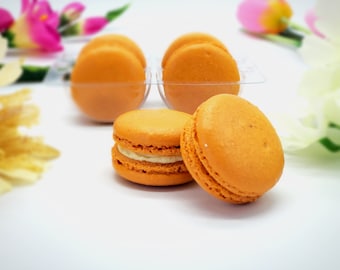 Può includere: Primo piano di quattro macarons arancioni, di cui due sono riempiti con crema bianca. I macarons sono disposti in un contenitore di plastica trasparente.