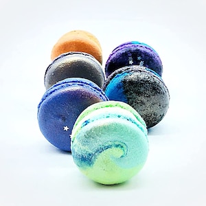 May include: A collection of six colorful macarons with a variety of designs. The macarons are arranged in a row, with the largest macaron in the front and the smallest macaron in the back. The macarons are all different colors, including blue, green, purple, and brown.