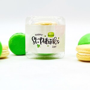 K&ouml;nnte beinhalten: Ein gr&uuml;nes Macaron mit wei&szlig;em Frosting in einem durchsichtigen Plastikbeh&auml;lter mit einem wei&szlig;en Etikett, auf dem "Happy St. Patrick's Day" steht.