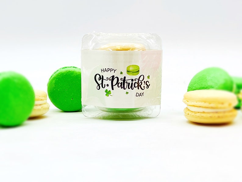 K&ouml;nnte beinhalten: Ein gr&uuml;nes Macaron mit wei&szlig;em Frosting in einem durchsichtigen Plastikbeh&auml;lter mit einem wei&szlig;en Etikett, auf dem "Happy St. Patrick's Day" steht.
